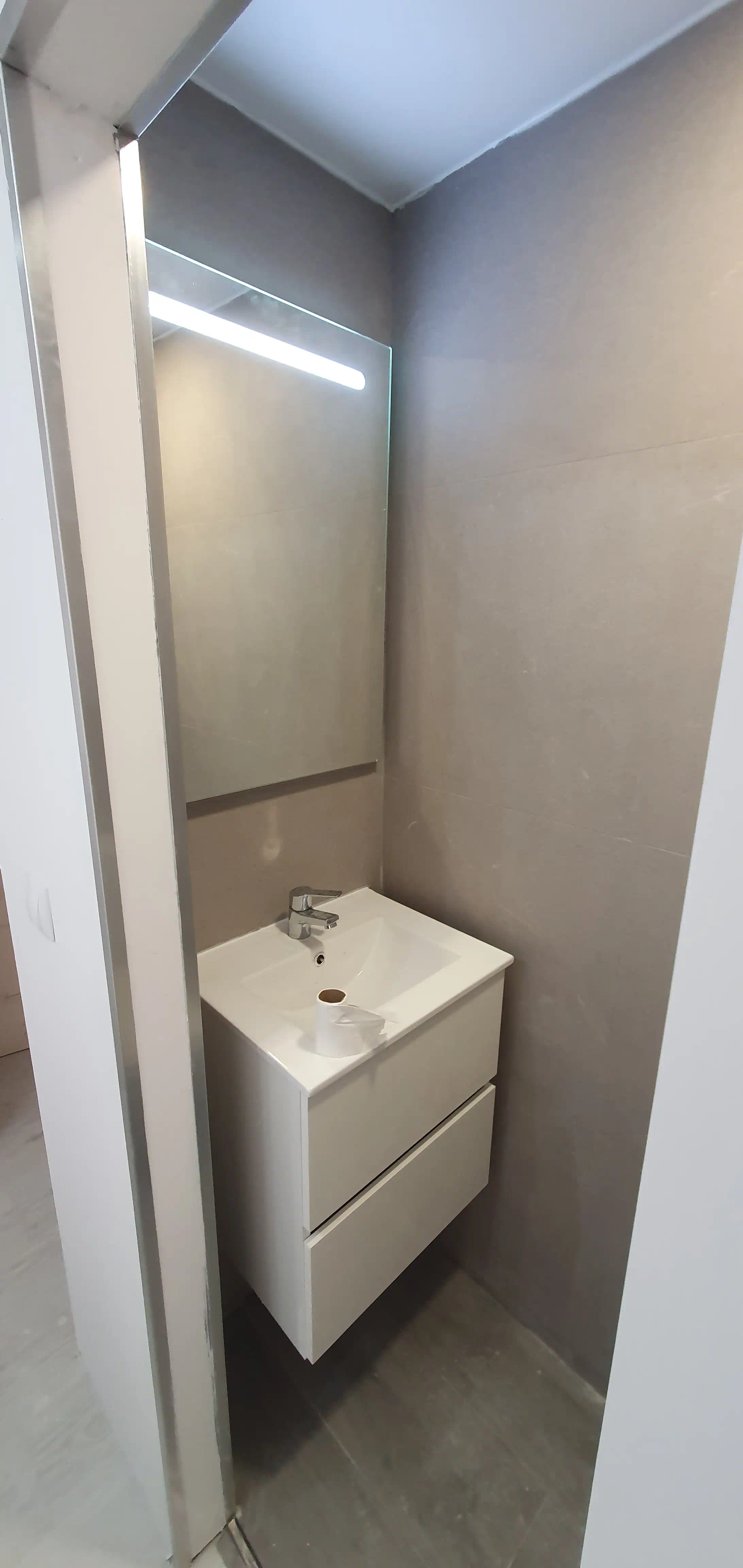 Revestimiento en porcelanato gris cemento 60x60 y suelo efecto madera en aseo adaptado