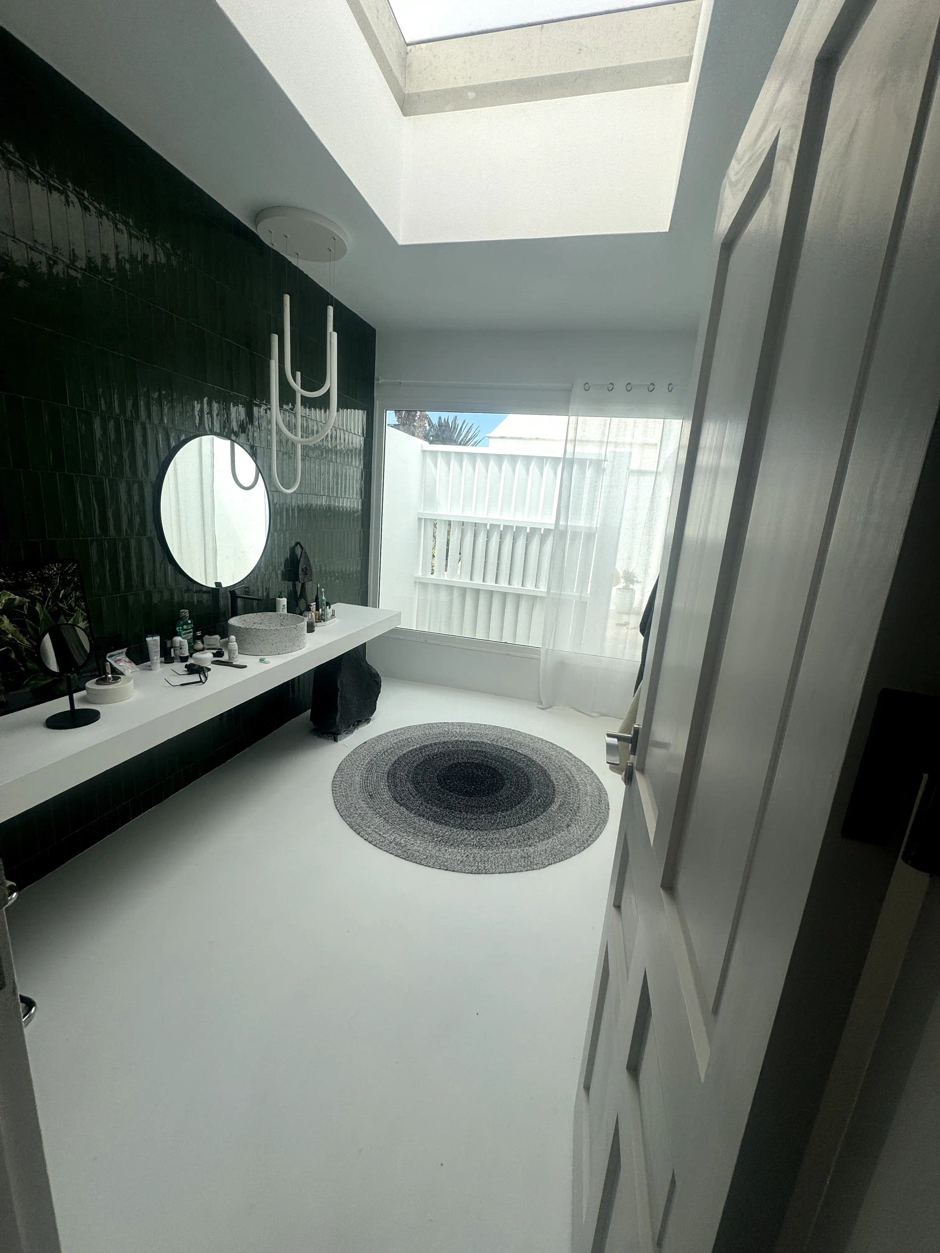 Zona de lavabo con encimera flotante, porcelanato tipo metro verde y piedra volcánica desde otro ángulo